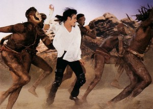 Michael Jackson danse en chemise blanche et en pantalon noir dans le sable avec un groupe de danseurs tribaux africains dans l'un des clips réalisés par John Landis, Black or White.