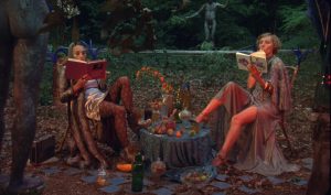 Deux femmes lisent autour de part et d'autre d'une petite table de jardin, scène baignée dans une étrange lumière orange du film Hormona de Bertrand Mandico.