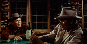 Glenn Ford joue aux cartes avec un camarade dans un saloon, le visage à moitié plongé dans la pénombre, scène du film L'homme de nulle part.