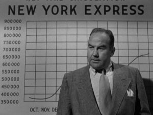 L'éditeur Mark Chapman la mine renfrognée devant le tableau représentant la chute des ventes du journal New-York Express, scène du film L'inexorable enquête.