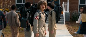L'équipe de Ghostbuster enfant, en uniforme, devant un lycée, l'un d'entre eux se tourne vers nous, inquiet, illustration pour notre article sur la tendance vintage de Hollywood.