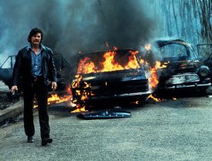 Charles Bronson s'éloigne de deux voitures en flamme, scène du film Le flingueur.