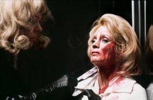Angie Dickinson le visage en sang dans un ascenseur, face à elle le tueur travesti vêtu d'un manteau de cuir noir, scène du film Pulsions de Brian De Palma.