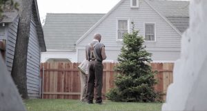 Eric Judor en jardinier vu de dos, au fond d'un jardin de banlieue résidentielle américaine, scène du film Wrong.