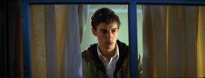 L'acteur Daniel Spencer cadré en rapproché-poitrine entre deux rideaux, derrière une fenêtre dans le film The Great Ecstasy of Robert Carmichael.