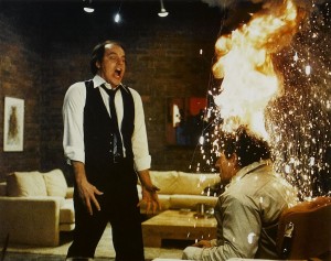 Le méchant du film Scannars comme en transe face à un homme, assis, dont la chevelure prend feu, scène dans un salon cossu des années 70.