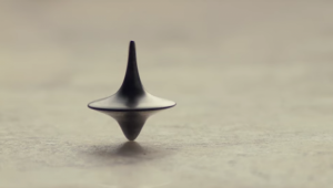 Une toupie tourne sur une table grise, gros plan issu du film Inception de Christopher Nolan.