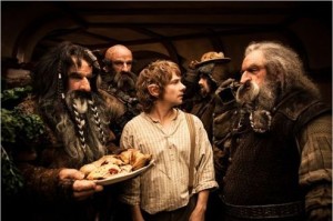 Bilbo entouré par un groupe de guerriers à nez pointus, dont l'un tient un plateau de victuailles, scène du film Le hobbit un voyage inattendu.