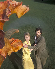 Un homme tente de retenir une femme qui s'approche, un peu effrayée d'une fleur géante dans le film La révolte des triffides.