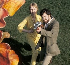 Un homme tente de retenir une femme qui s'approche, un peu effrayée d'une fleur géante dans le film La révolte des triffides.