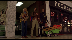 Les quatre héros du film Zombie - trois sont debout armés, le quatrième est blessé dans un petit chariot de jardin - attendant l'arrivée des morts-vivants dans le centre commercial du film Zombie.