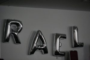 Les lettres du mot Raël formées sur un mur avec des ballons de baudruche gris.