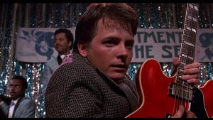 Marty sur scène, avec sa guitare, remarque quelque chose qui le stoppe hors-champ, scène du film Retour vers le futur pour notre article sur la tendance vintage de Holllywood.