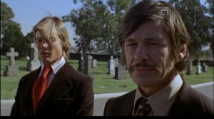 Arthur (Charles Bronson) au premier plan, Steve derrière lui, dans un cimetière sous un ciel bleu, scène du film Le flingueur.