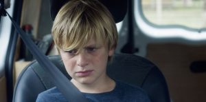 Julien sur le siège passager d'une voiture, les larmes aux yeux dans le film Jusqu'à la garde.