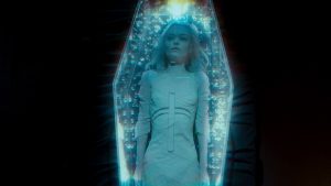 Une jeune femme blonde est dans un cercueil illuminé de bleu, scène du film Alien Crystal Palace pour notre critique.