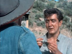 L'acteur Eugene Iglesias roule un billet, face à lui, de dos, un cow-boy à chemise en jean dont ne voit que l'épaule gauche, scène du film Le Bandit d'Edgar G. Ulmer.