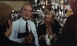 Jean Carmet en patron de bar derrière son guichet, en train de trinquer fièrement avec sa femme et deux clients que nous voyons en amorce, scène du film Dupont-Lajoie de Yves Boisset.