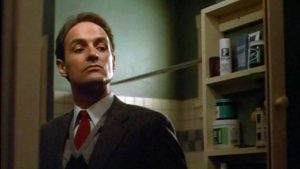 Terry O'Quinn, effrayant dans le film Le Beau-Père, scrute l'armoire à pharmacie de sa salle de bains.