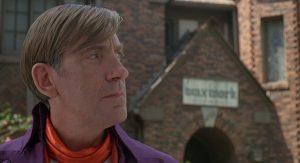 L'acteur Patrick Macneee souvieux dans la rue, la Waxwork en brique en arrière-plan, scène du film Waxwork.