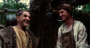 Le forgeron du village rit avec un étrange personnage médiéval sur le palier de son atelier, scène du film Jabberwocky.
