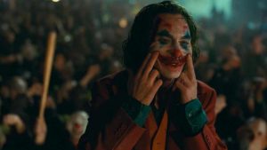 Le Joker mime son sourire, les doigits sur les lèvres, au milieu de la foule de révoltés du film Joker.