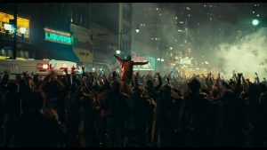 Le Joker exulte au milieu d'une émeute en pleine ville, les bras en croix.
