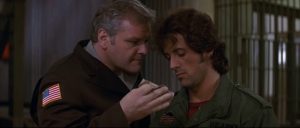 Un policier menaçant exige que John Rambo pose ses empreintes comme un criminel, scène dans la prison du film Rambo de 1982.