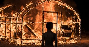 Scène de nuit dans le film Burning, un enfant vu de dos regarde sa maison brûler.