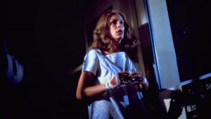Laurie Strode, jouée par Jamie Lee Curtis, en nuisette d'hopital dans une chambre juste éclairée par la lueur de la lune,, scrute l'arrivée du tueur Michael Myers.