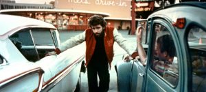 Le réalisateur George Lucas pose entre deux voitures des années 60 sur le tournage du film American Graffiti.
