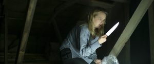 Cecilia refugiée dans un grenier avec un couteau, recroquevillée sur elle-même, scène du film Invisible Man.