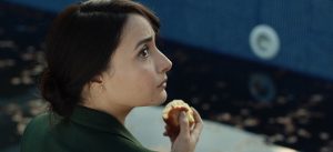 S, jouée par Souhir Ben Amara, est assise dans un environnement indicernable,elle regarde vers la droite d'un air inquiet, elle tient une pomme croquée dans la main, scène du film tunisien Sortilège.