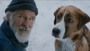 Sur fond enneigé, le chien Buck regarde John Thornton, interprété par Harrison Ford, scène du film L'Appel de la Forêt.