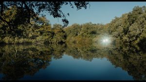 Un étang calme entouré d'arbre, sous un ciel bleu, scène du film Sortilège.