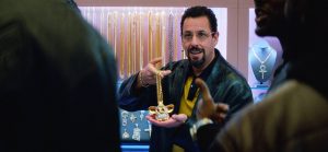 Adam Sandler face à deux clients, tente de vendre un pendentif dans sa bijouterie, scène du film Uncut Gems.