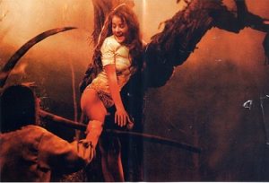 Une jeune femme en culotte fuit un homme qui tente de la tuer avec une grande faux, en grimpant sur une branche d'arbre, scène dans les tons sepia, du film Le crocodile de la mort.
