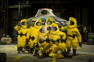 Un groupe en combinaison de protection radioactive jaune pose devant un vaisseau spatial, dans un hangar, scène du film Shaun le mouton : la ferme contre-attaque.