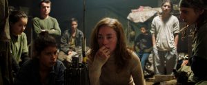 L'actrice Julianne Nicholson qui joue Sara Watson, un docteur en otage réfléchit dans une tente sous le regard de quelques membres du groupe rebelle armé, scène du film Monos.