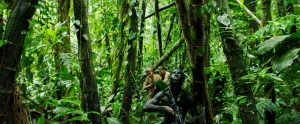 Un guerillero peint en noir pour le camouflage avance dans la foret amazonienne, fusil d'assaut dans les mains, scène du film Monos.