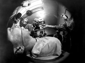 Angoissante image en noir et blanc et fish eye, une équipe de médecins se penche sur un malade dans un bloc opératoire, scène du film L'opération diabolique.