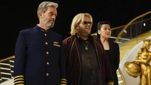 Le Capitaine Ryan Clark guide un visiteur, homme blond assez gros, lunettes de soleil, chaîne en or, et son assistante asiatique sur le pont de son vaisseau qui ressemble à un bateau, scène de la série Avenue 5.