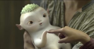 Le mignon bébé monstre Wuba dans les bras d'une femme, il est blanc avec une touffe de cheveux verts, et des oreilles pointues.
