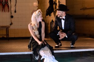 Lula et Gaspard en tenus de soirée (costume et chapeau haut de forme pour lui, robe noire élégante pour elle), se regardent en souriant au bord d'une piscine, scène du film Une sirène à Paris.