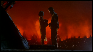 Un homme et une femme debout face à face, en fond une image de Shanghai en feu, de nuit, scène du film Shanghai Blues.