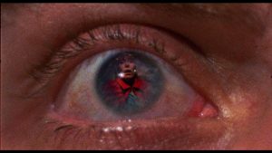 Une silhouette rouge se reflète dans une rétine, plan du film Patrick.