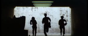 Trois silhouettes d'hommes courent vers la lumière du jour et la sortie d'un tunnel sombre, scène du film L'enfer des armes.