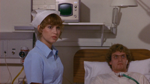 Une infirmière est à côté de Patrick, allongé dans son lit, tous deux regardent sur la droite, inquiets, scène du film Patrick.