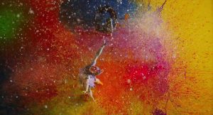 Vue en plongée, une jeune femme saute au milieu d'une bombes de peintures rouge, violette, bleue, et jaune, scène du film Antiporno pour notre article sur le roman porno japonais édité chez Elephant Films