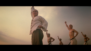 En contre-plongée, des moines shaolin s'entraînent, le poing levé vers le ciel, scène du film Il était une fois en Chine.